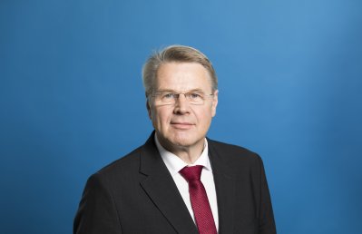 Staatssekretär Bottermann freundlich lächelnd - Hintergrund blau.