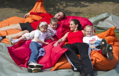 Mehrere Kinder ruhen sich mit ihrer Trainerin nach dem Sport auf großen, roten und orangefarbenen Kissen aus.