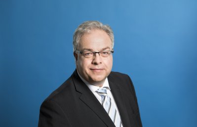 Staatssekretär Dr. Patrick Opdenhövel freundlich lächelnd vor blauem Hintergrund.