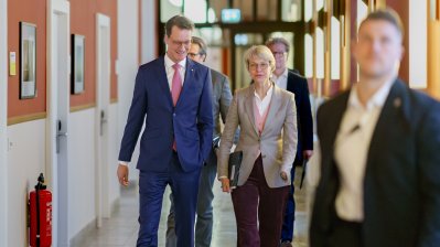 Ministerpräsident Hendrik Wüst und Ministerin Feller gehen auf einem Flur zur Pressekonferenz