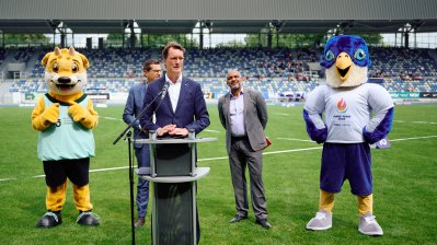 MP Wüst hält ein Grußwort, im Hintergrund das Maskottchen