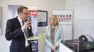 Ein Mitarbeiter zeigt der Ministerpräsidentin etwas vor einem Schaukasten