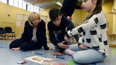 Ministerpräsidentin Hannelore Kraft sitzend auf dem Turnhallenboden mit Schülerinnen und Schülern mit Themenpuzzle 