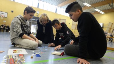 Ministerpräsidentin Hannelore Kraft sitzend auf dem Turnhallenboden mit Schülerinnen und Schülern mit Themenpuzzle 