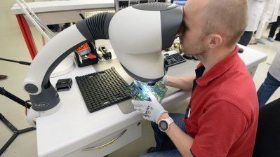 Ein Mitarbeiter betrachtet eine Platine unter einem Mikroskop