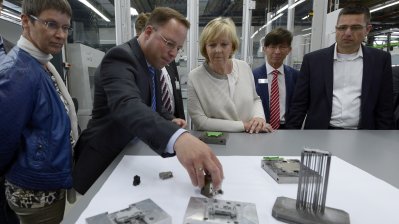 Ministerpräsidentin Kraft betrachtet unterschiedliche Produktionserzeugnisse aus Metall auf einem Tisch