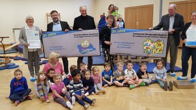 Gruppenfoto mit Staatssekretärin Andrea MIlz, vor ihr sitzen die Kinder der Eichhörnchen-Gruppe auf dem Turnhallenboden.