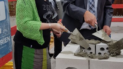 Staatssekretärin Andrea Milz spachtelt Mörtel zwischen die Mauersteine bei der Grundsteinlegung der Sporthalle Lüdinghausen.