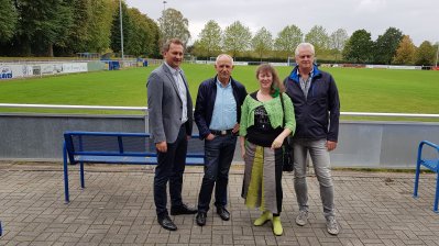 Staatssekretärin Andrea Milz mit Mitgliedern des SV Herbern vor einem Rasen-Fußballplatz.