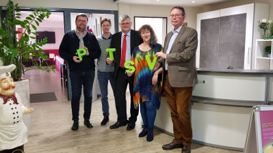 Staatssektretärin Milz hält mit drei Mitgliedern des Post-Telekom-Sportverein 1925 Aachen e.V. die vier Buchstaben P, T, S und V in grün jeweils in den Händen in Richtung Kamera..