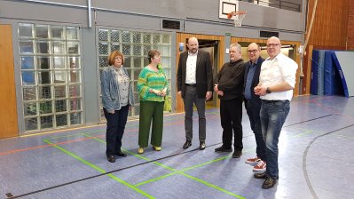 Staatssekretärin steht mit Mitgliedern des Handballvereins in einer Sporthalle.