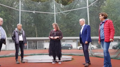 Staatssekretärin MIlz steht mit 4 Vereunsnutgkuedern an einer Hammerwurf-Sportstätte, hinter ihnne befindet sich ein Auffang-Stahlnetz.