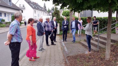 Staatssekretärin Milz steht im Kreis mit anderen Personen, während eine Dame etwas vorträgt. Sie befinden sich draußen auf einem Bürgersteig vor einem Treppenaufgang, beidseitig mit Geländern.