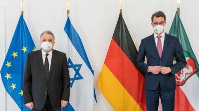 Zwei Männer stehen vor den Flaggen der EU, Israel, Deutschland und NRW