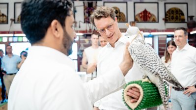 Ministerpräsident Wüst steht in einem Geschäft und hält einen großen weißen Vogel auf dem Arm