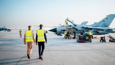 Ministerpräsident Wüst und ein Soldat gehen auf dem Rollfeld auf einen Kampfjet zu