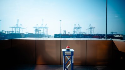 Ein roter großer Button auf einem Tisch, im Hintergrund ein Hafen