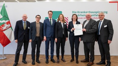 MP Wüst und Minister Lauman posieren mit Förderbescheidempfängern und eine Urkunde für ein Foto