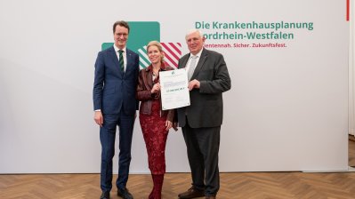 MP Wüst und Minister Lauman posieren mit Förderbescheidempfängern und eine Urkunde für ein Foto