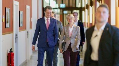 Ministerpräsident Hendrik Wüst und Ministerin Feller gehen auf einem Flur zur Pressekonferenz
