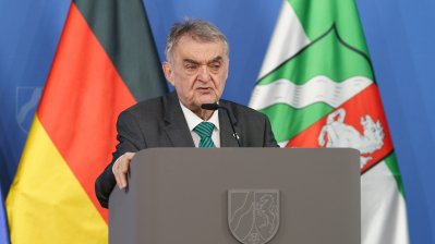 Minister Reul spricht an einem Rednerpult vor Flaggen