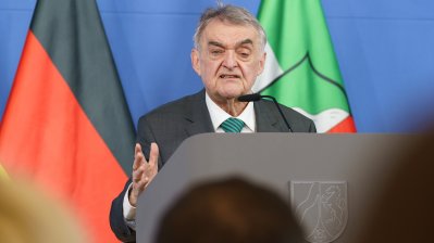 Minister Reul spricht an einem Rednerpult vor Flaggen