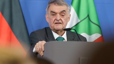 Minister Reul spricht an einem Rednerpult vor Flaggen