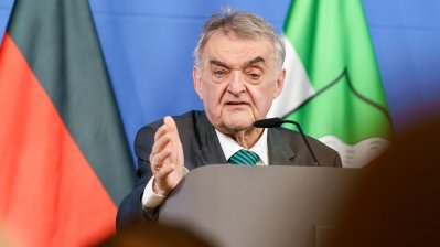 Minister Reul spricht an einem Rednerpult vor Flaggen