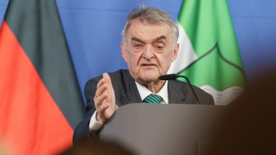 Minister Reul spricht an einem Rednerpult vor Flaggen