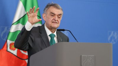 Minister Reul spricht an einem Rednerpult vor Flaggen