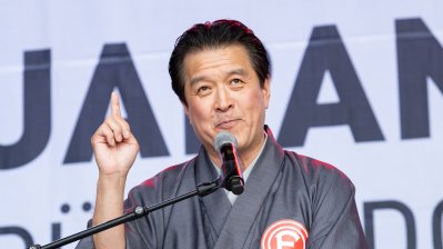 Ein Mann in traditionell japanischer Kleidung hält auf der Bühne einer Ansprache