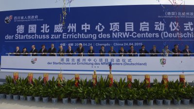 Viele Teilnehmer halten ein Geländer vor einer großen Plakatwand mit dem Titel der Veranstaltung