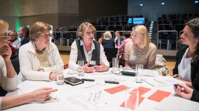 Mehrere Damen im Gespräch an einem runden Tisch sitzend.