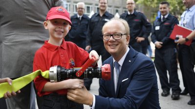 Landtagspräsident André Kuper und ein junger Feuerwehrmann halten einen Feuwehrschlauch