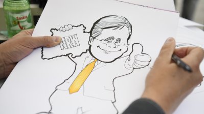 Ein Karikaturist zeichnet Ministerpräsident Armin Laschet mit gelber Krawatte und gehobenem Daumen
