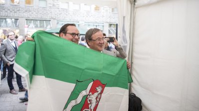 OB Kufen und Ministerpräsident Laschet halten eine NRW-Flagge in die Kamera