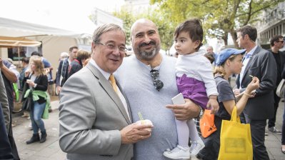 Ministerpräsident Armin Laschet mit Eis in der Hand und ein Vater mit Kind auf dem Arm posieren für ein Foto