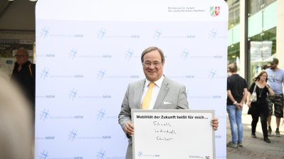 Ministerpräsident Laschet hält ein ausgefülltes Schild in die Kamera: Mobilität heißt für mich... "schnell, individuell, sauber"