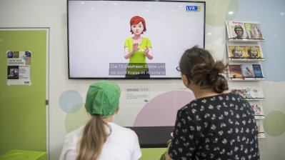 Eine Mutter schaut mit ihrer Tochter auf einen Monitor, auf dem die 13 kreisfreien Städte des Rheinlands erklärt werden