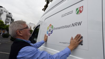 Ein älterer Herr beklebt den Ehrenamtstourbus seitlich mit dem Ehrenamtstour.NRW-Log