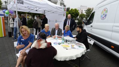 Ehrenamtstour-Veranstaltung: Eine Gruppe sitzt an einem runden Tisch, rechts steht der Ehrenamtstourbus, hinten steht ein Pavillonzelt.