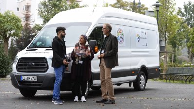 Eine Dame und zwei Herren im Gespräch vor dem Ehrenamtstourbus stehend.