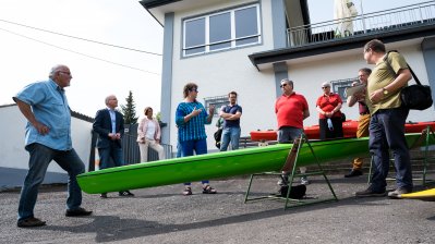 Staatssekretärin Milz mit Vereinsmitgliedern vor dem Vereinshaus, vor Ihnen ein langes, grünes Kanu aufgebockt.