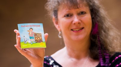 Staatssekretärin Andrea Milz hält das Pixi-Buch mit ihrer rechten Hand vor sich für die Kamera.