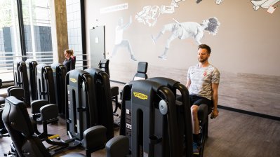 Zwei Trainierende sitzen auf fitnessgerten in einem Fitnessraum.