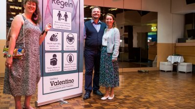 Staatssekretärin Milz steht mit einem Paar an der Hygiene-Plakatwand des Tanzhauses.