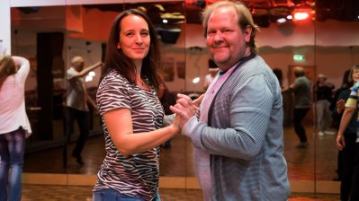 Ein tanzendes Paar,, im Hintergrund ders Tanzsaales sieht man noch mehr tanzende Paare.