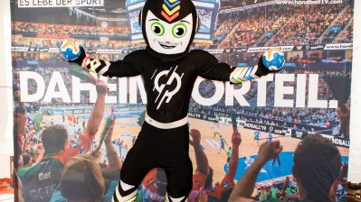 Im Vodergrund ein schwarz-wießes Maskottchen, im Hintergrund das Stadion