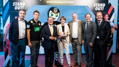 MInisterpräsident Laschet mit mehreren Personen im Halbkreis sthend, hinter ihm das Maskottchen.