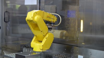 Ein gelber Roboter-Arm hinter einer Glasscheibe
